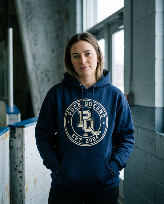 The Crest Hoodie in navy with the cream Puck Queens crest, worn in an arena corridor